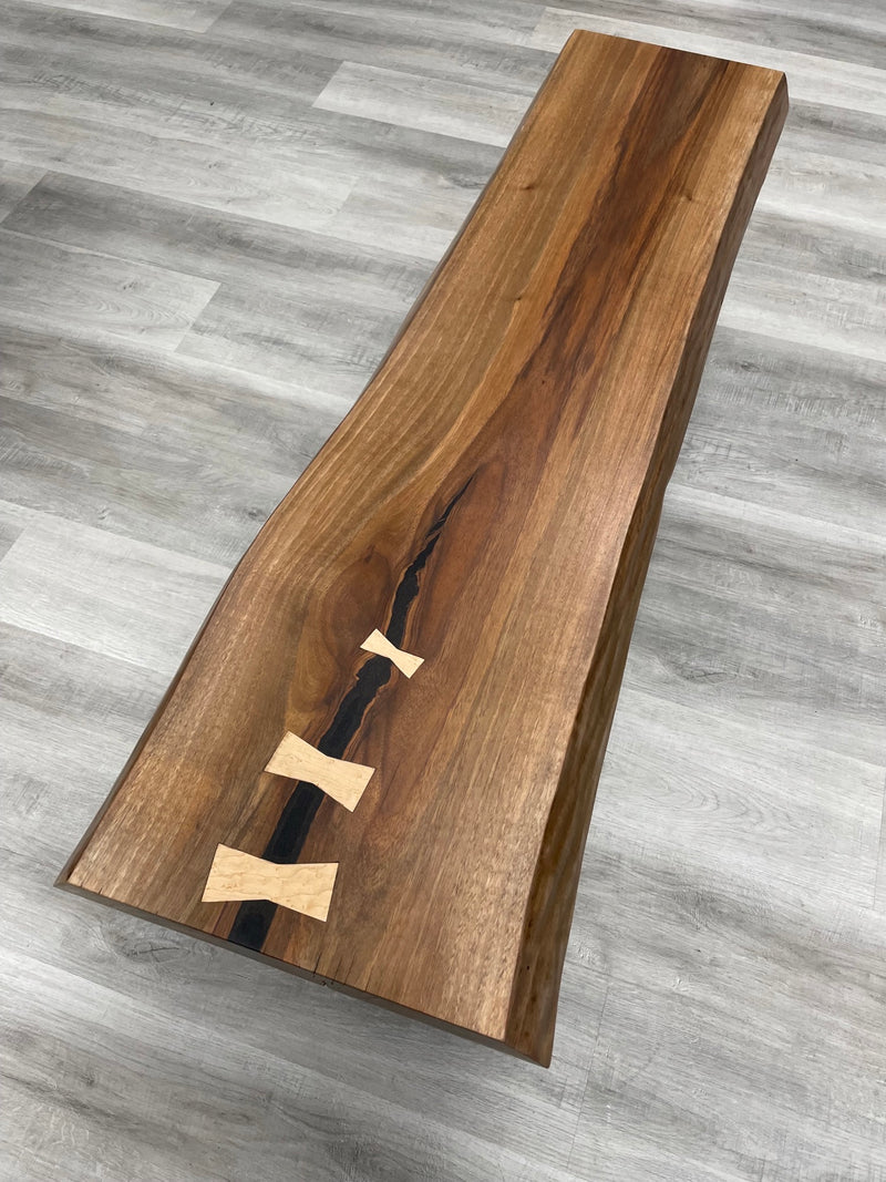 Solid black walnut bench with a live edge and maple bowties. Top view.