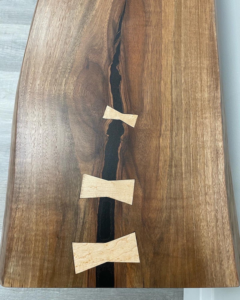 Solid black walnut bench with a live edge and maple bowties . Close up.