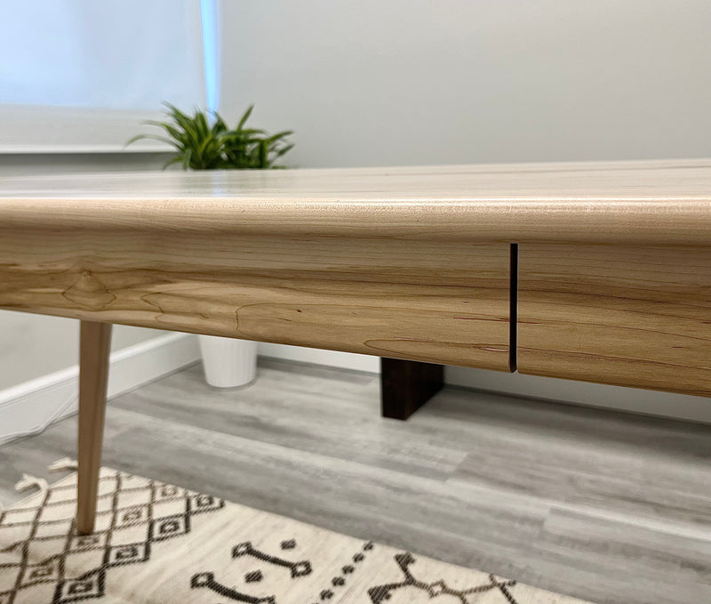 Solid maple desk with a hidden drawer and tapered legs in a natural finish.  Close up of a  closed drawer.