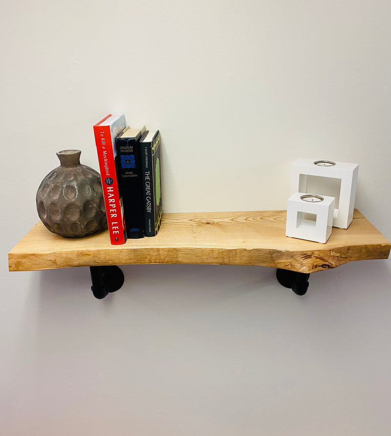Natural edge solid wood shelf with books and decor and black pipe brackets