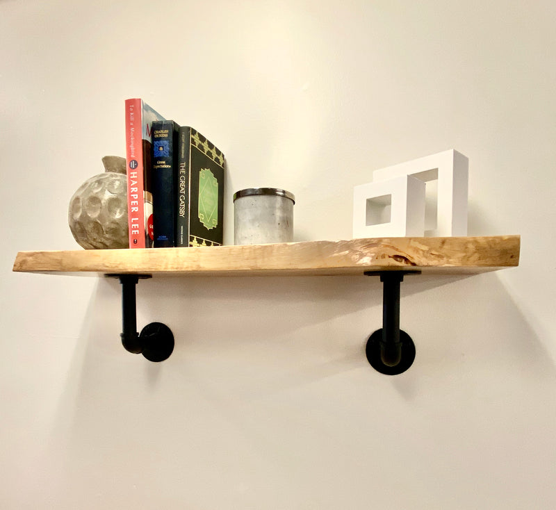 Natural edge solid wood shelf with books and decor and black pipe brackets